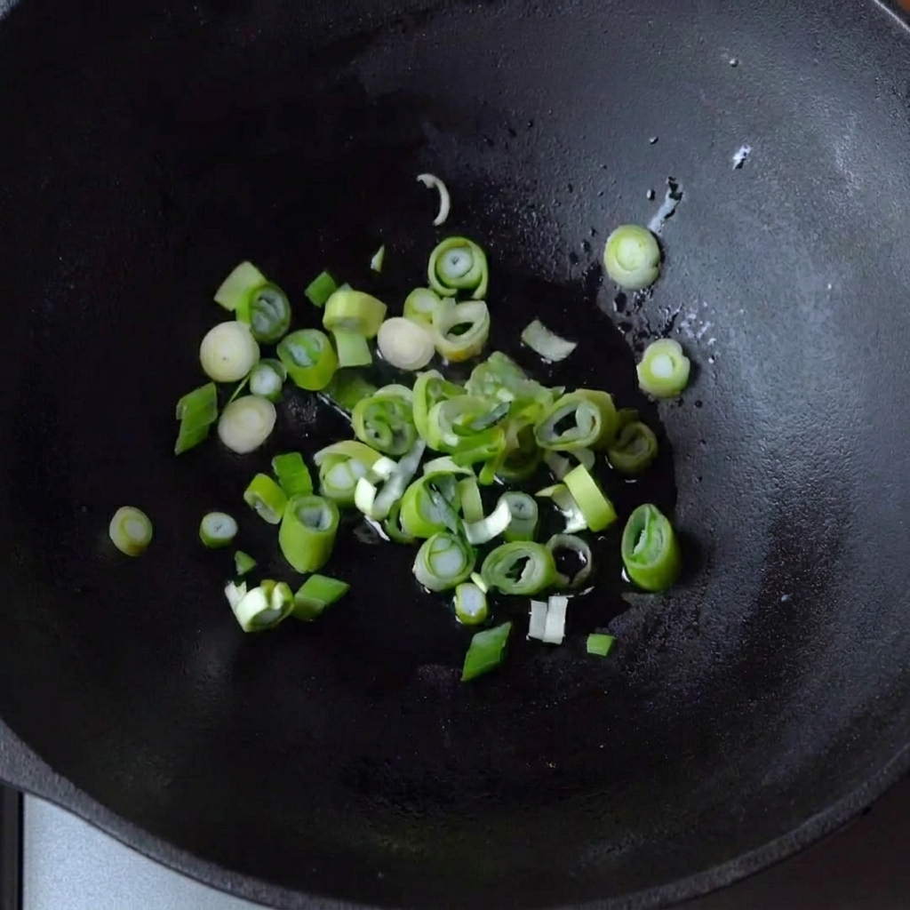 Des oignons verts grésillant dans un fond dhuile au sein dun wok en fonte.