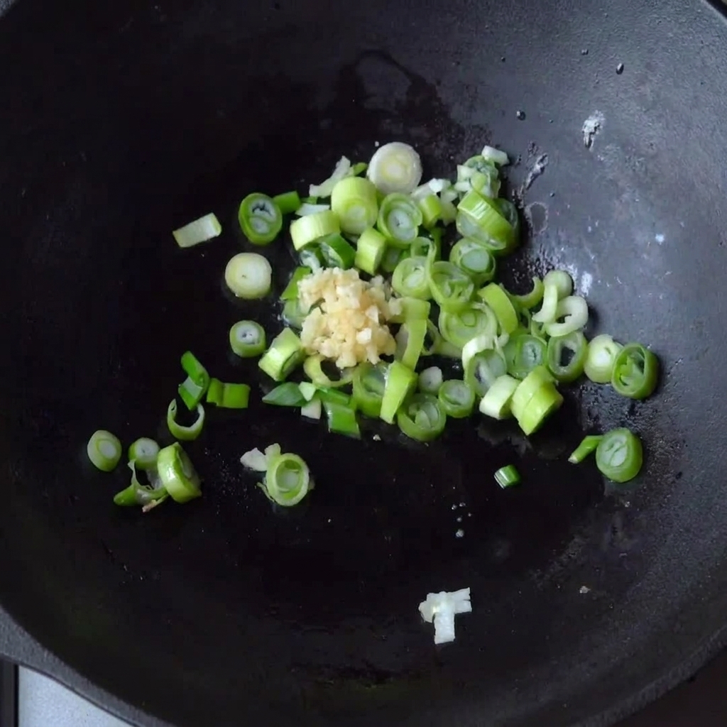 De lail émincé ajouté dans la poêle contenant déjà les oignons verts en cours de cuisson.