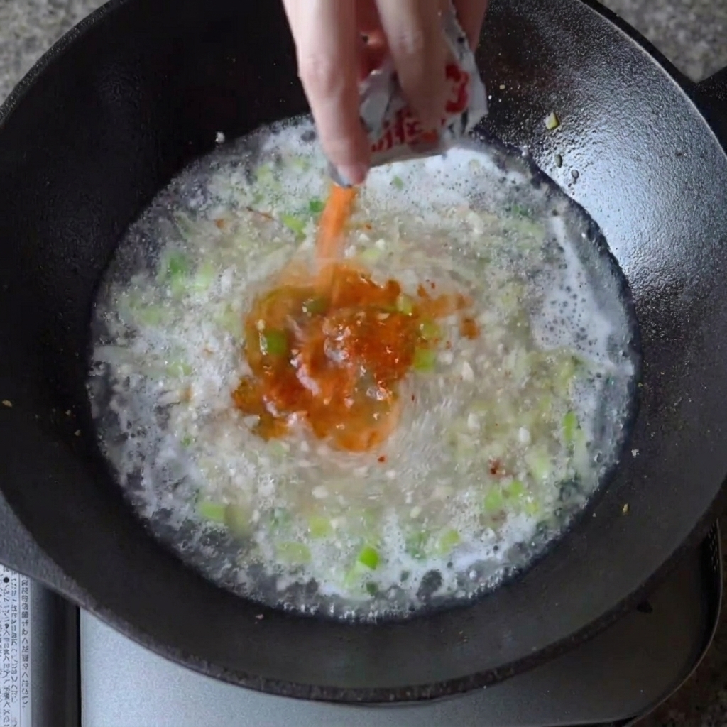 La poudre dassaisonnement pour ramen saupoudrée dans le bouillon frémissant du wok.