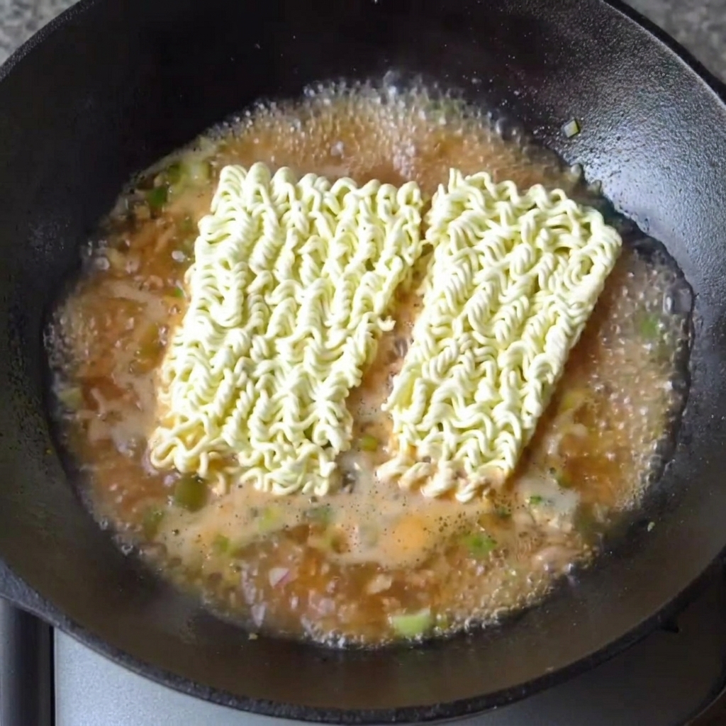 Deux blocs de nouilles ramen séchées reposant dans le bouillon bouillant et parfumé.