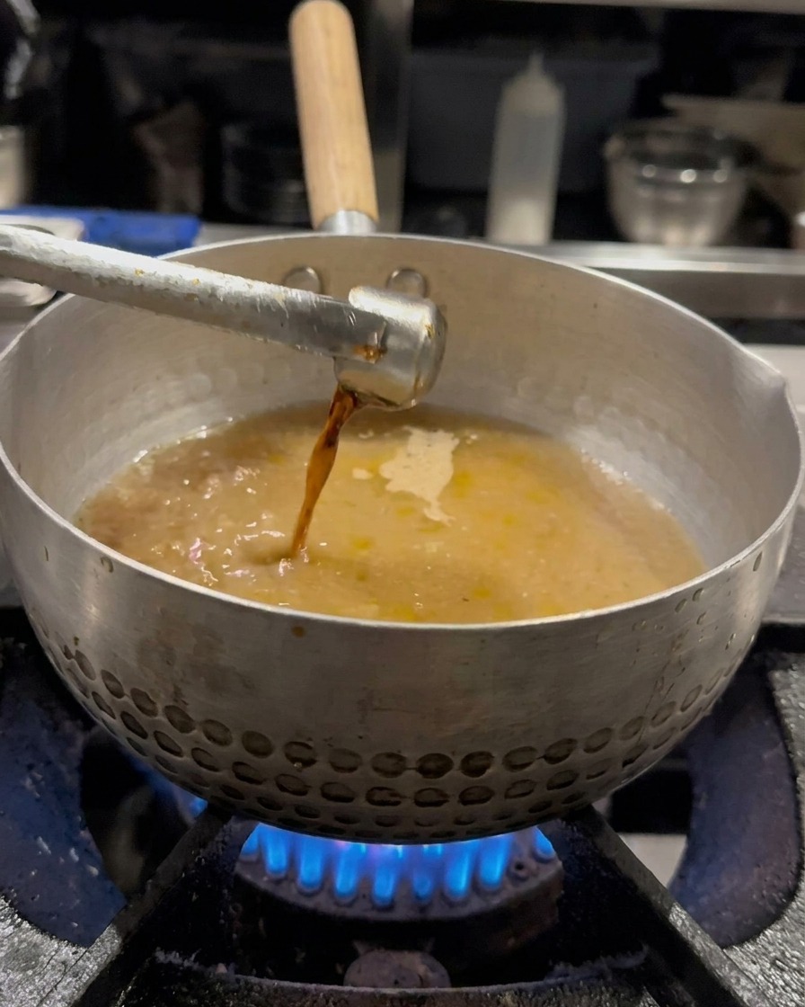 Sauce soja versée dans la casserole remplie de bouillon et mélangée avec un fouet.