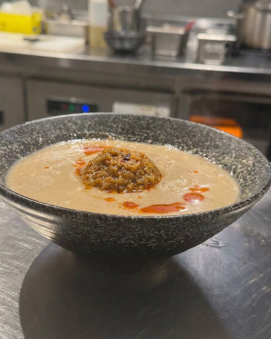 Un bol de Tan Tan Ramen à la japonaise avec un bouillon crémeux, surmonté dun dôme de viande hachée et dhuile pimentée rouge vif versée par-dessus.