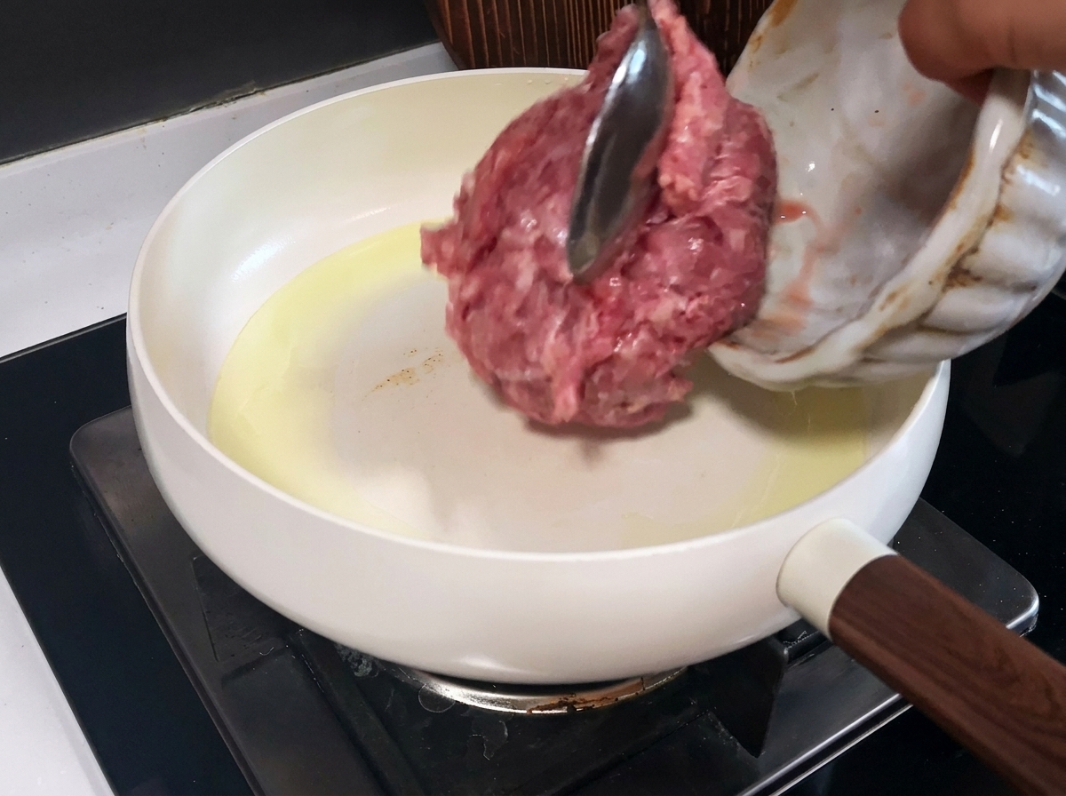 Porc haché en train de cuire dans une poêle blanche, montrant des morceaux bien dorés.