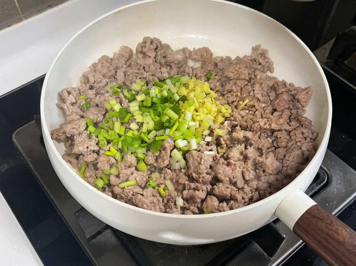 Porc haché dans une poêle mélangé avec des aromates hachés, de la pâte de haricots et de la pâte de soja.
