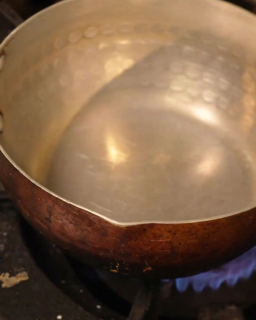 Une casserole en métal martelé contenant du liquide chauffe sur un brûleur de cuisinière.