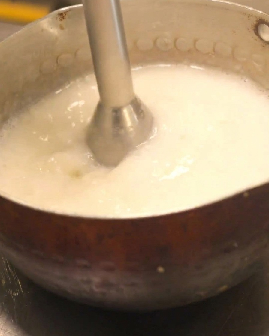 Un mixeur manuel utilisé pour créer une mousse crémeuse dans une casserole de soupe de poulet paitan.