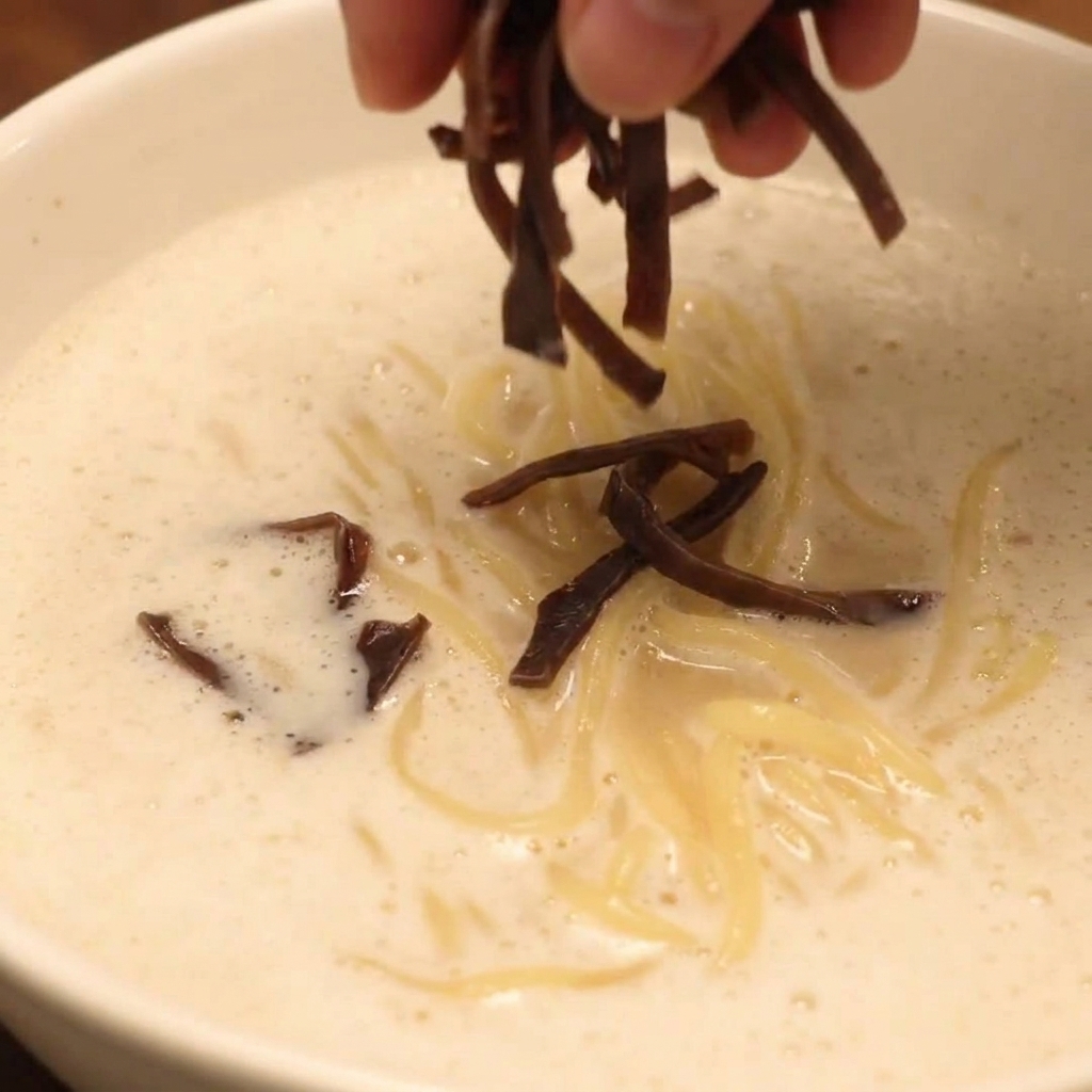 Un bol de Ramen au Poulet Paitan en Mousse entièrement assemblé, garni de chashu, de champignons et de légumes frais.