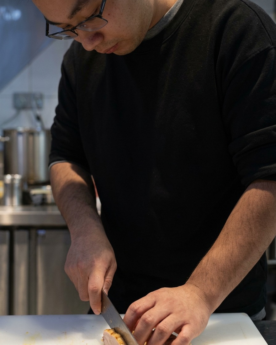 Couteau tranchant le poulet chashu cuit sur une planche.