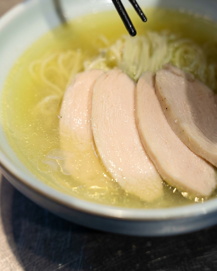 Baguettes déposant des tranches de poulet chashu sur un bol de ramen.