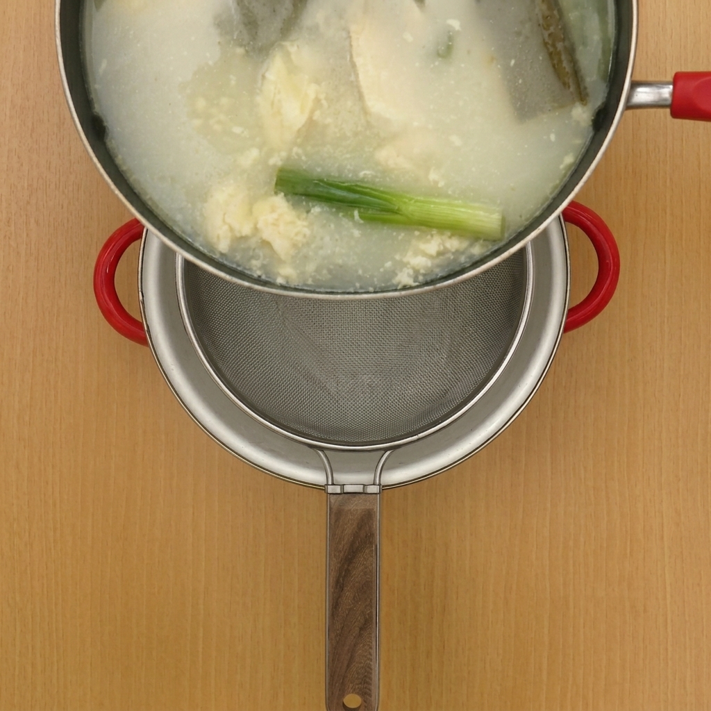 Bouillon de poulet chaud versé à travers un tamis métallique dans une marmite propre.