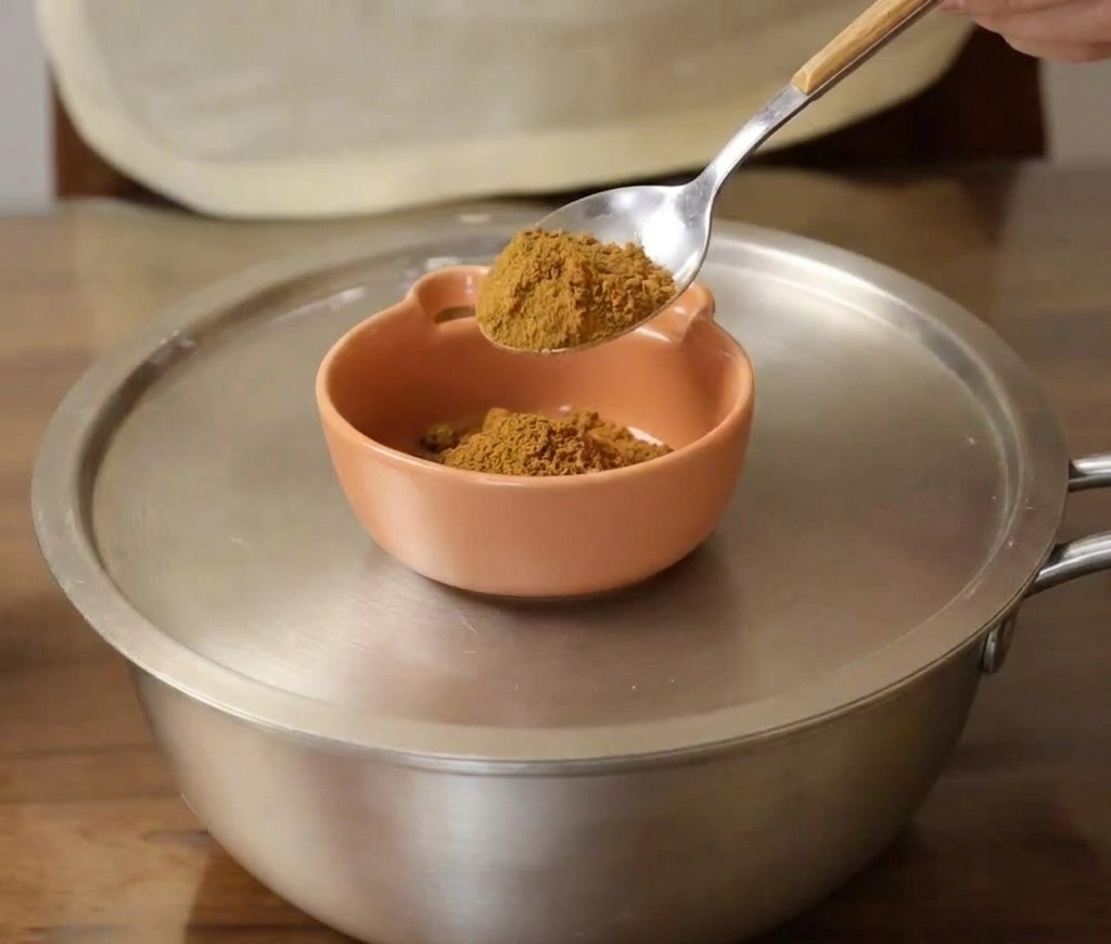 Une cuillère de moutarde en poudre ajoutée dans un petit bol en céramique orange.