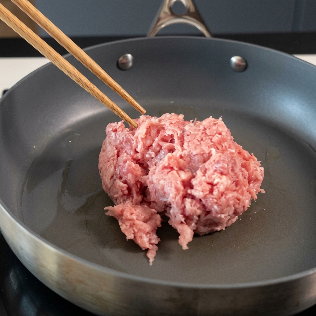 Porc haché remué dans une poêle antiadhésive avec des baguettes.