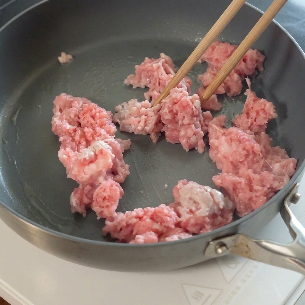 Ail émincé ajouté au porc haché cuit dans la poêle.