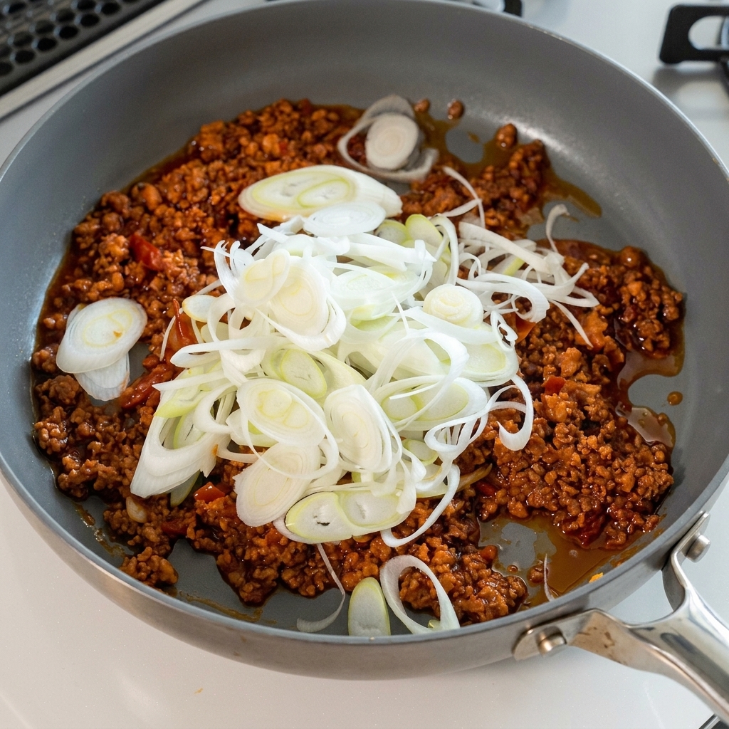 Une grande quantité doignons verts hachés ajoutée à la sauce à la viande.