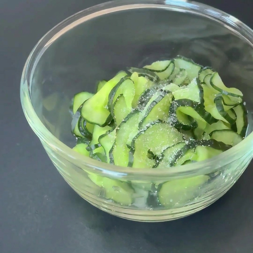 Tranches de concombre dans un bol en verre assaisonnées avec du sucre et du vinaigre de cidre.