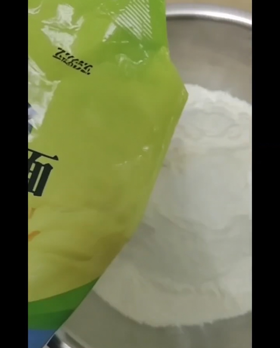 Vue rapprochée de leau versée dans un grand bol contenant de la farine, avec une cuillère visible pour mélanger.