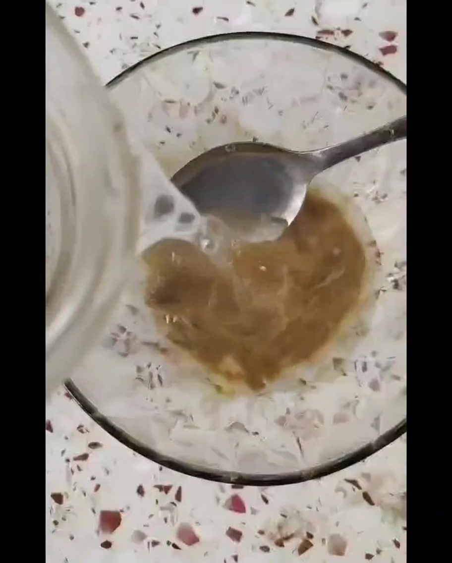 Un petit bol en verre contenant une sauce brune épaisse mélangée avec une cuillère en métal.