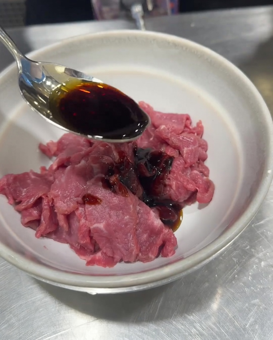 Bœuf cru tranché dans un bol, assaisonné avec de la sauce soja, du sel, du poivre et de la fécule de maïs.