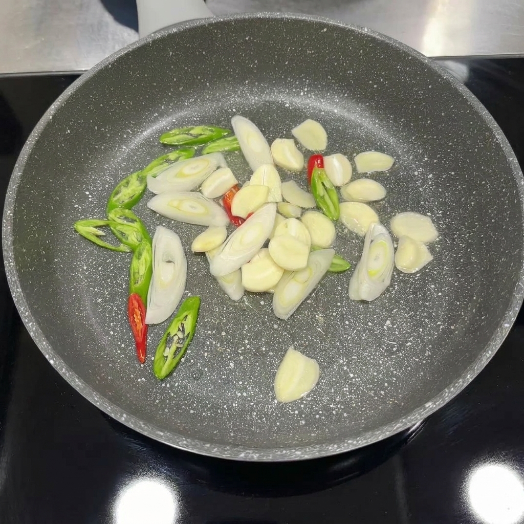 Ail, piment et oignons verts tranchés cuisant dans une poêle jusquà ce quils soient aromatiques.