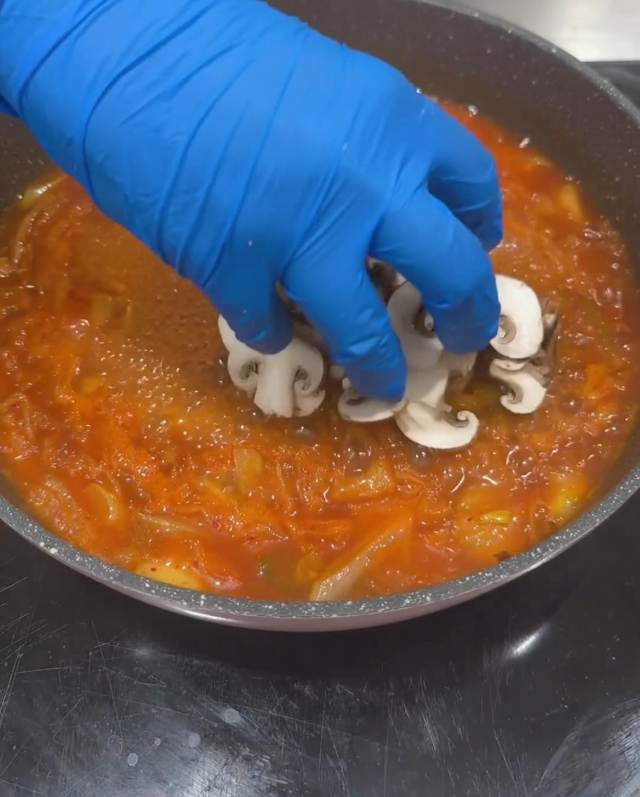 Champignons shiitake, courgettes et dés de tofu ajoutés dans la base de soupe au kimchi bouillante.
