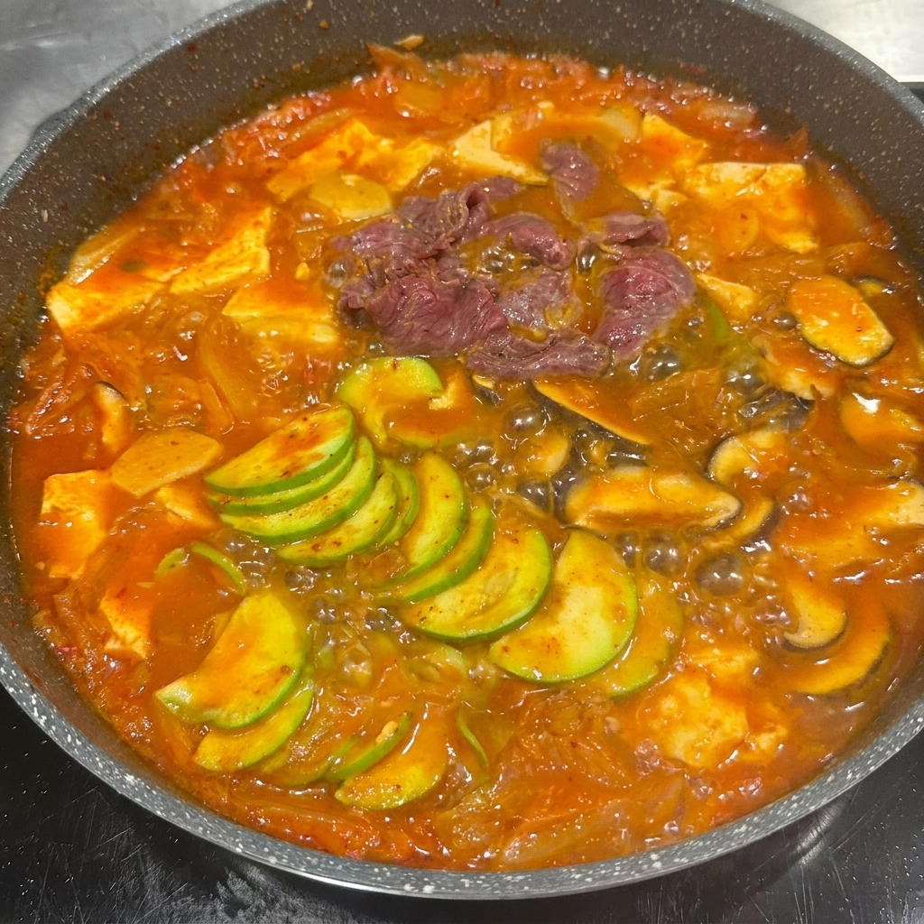 Tranches de bœuf mariné placées dans la casserole avec les légumes mijotés et le bouillon de kimchi.