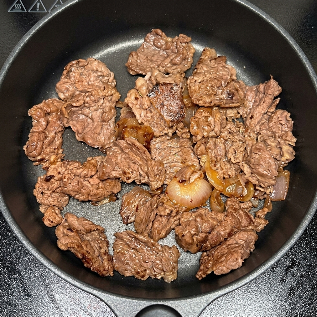 Morceaux de kimchi ajoutés dans la poêle avec le bœuf et les oignons.
