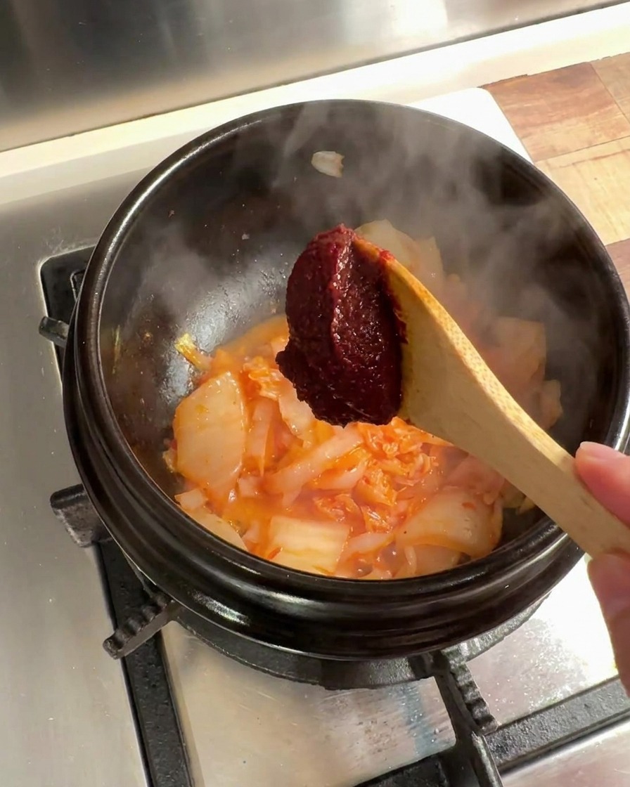 Une cuillère de pâte de piment coréenne ajoutée au mélange de kimchi et doignons.
