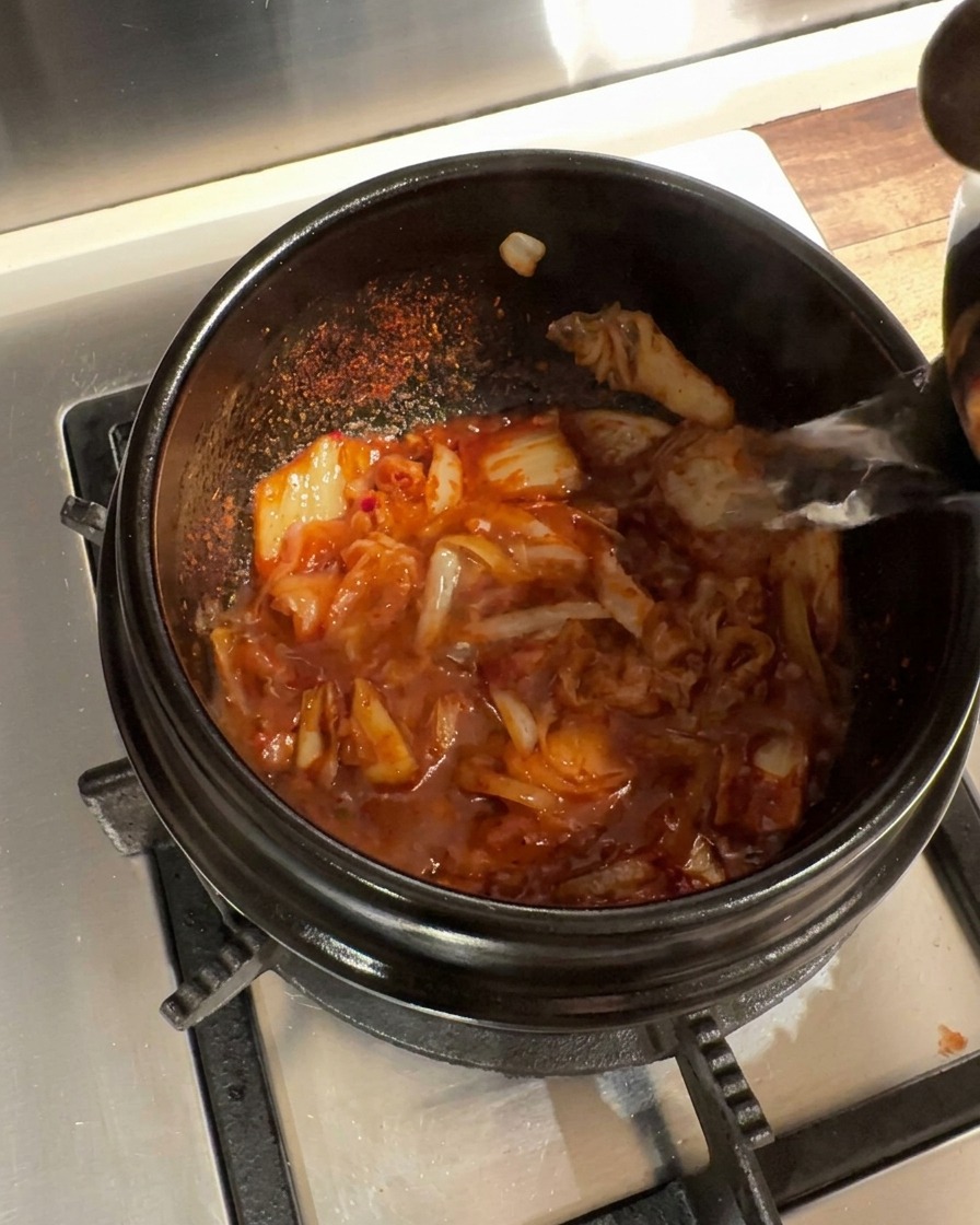 De leau bouillante est versée dans le poêlon contenant la base de kimchi assaisonnée.