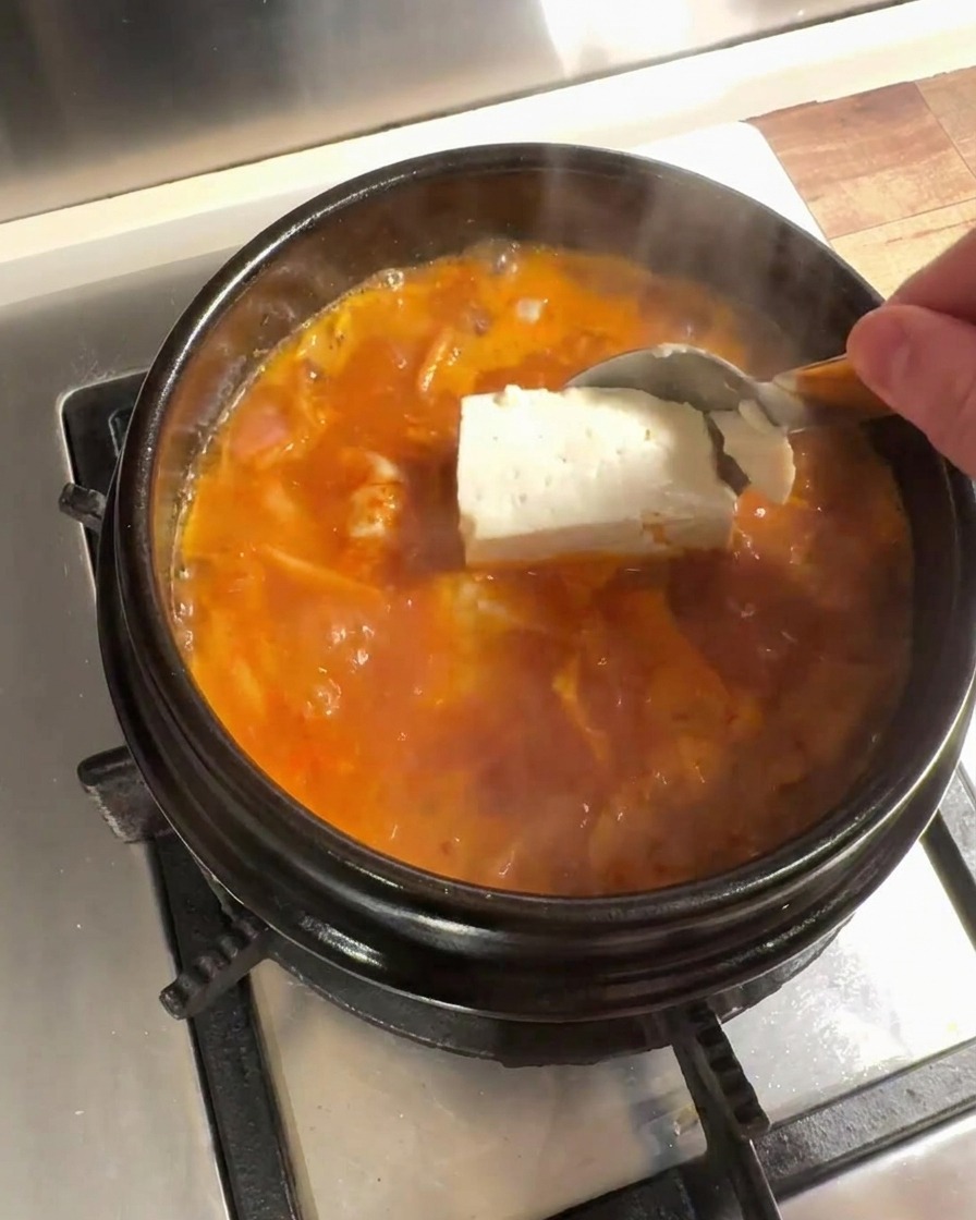 De gros morceaux de tofu frais ajoutés dans le bouillon de kimchi frémissant.