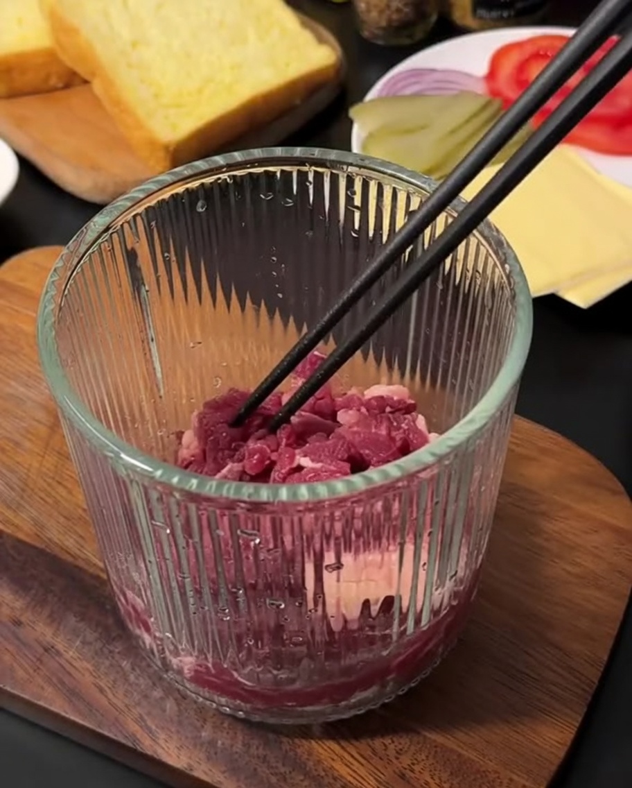 Bœuf haché cru et frais dans un hachoir manuel en verre, prêt à être mixé.