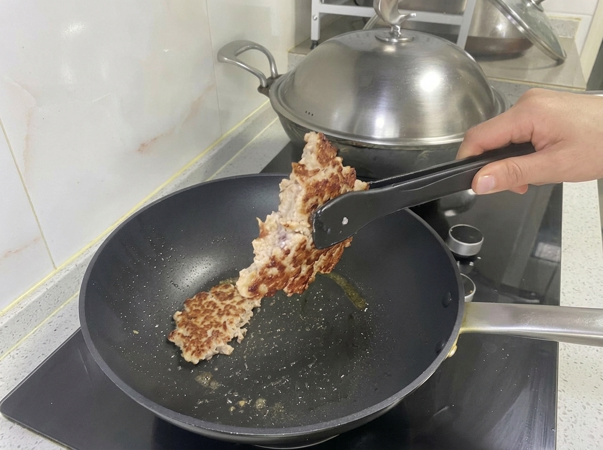 Galette de porc dorée soulevée de la poêle avec une pince.