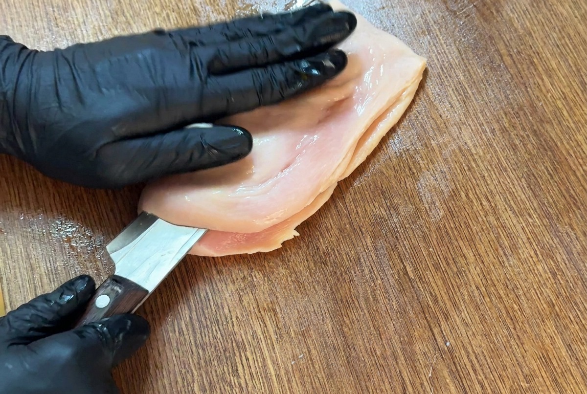 Un couteau tranchant coupant horizontalement un blanc de poulet sur une planche à découper pour louvrir en portefeuille.