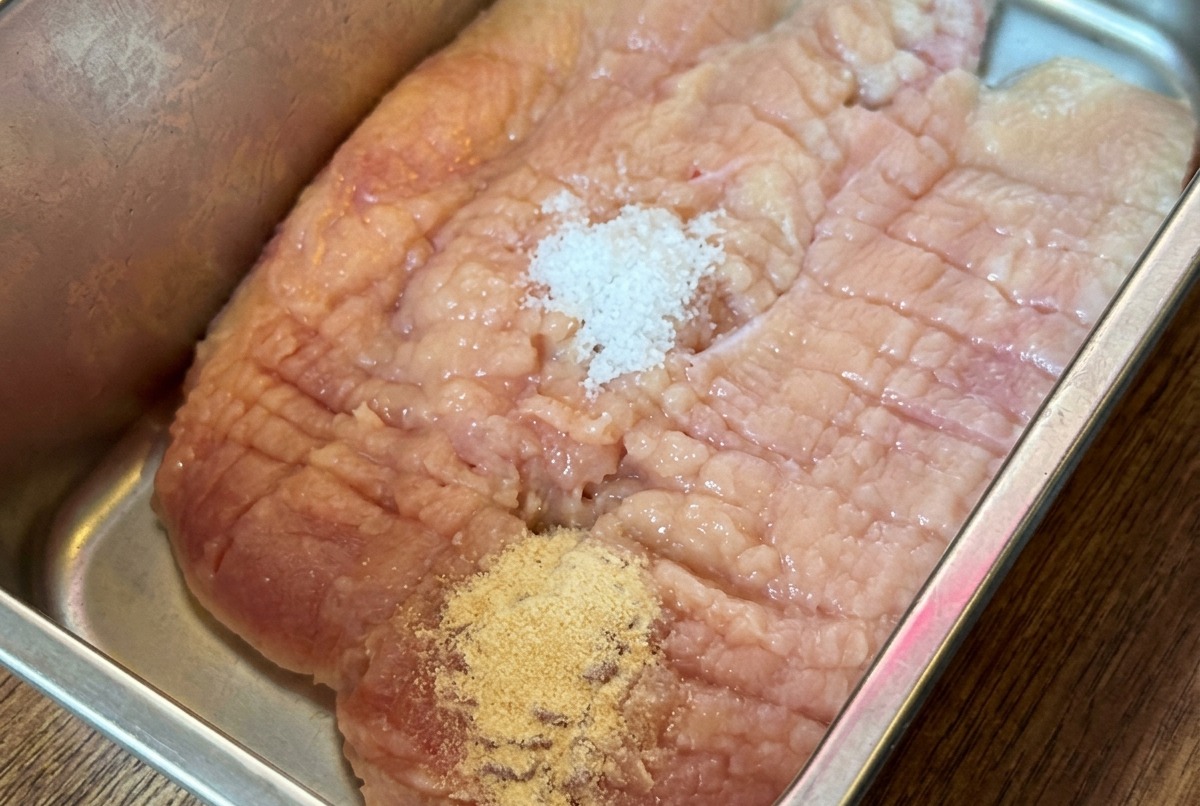 Un blanc de poulet cru dans un plateau en métal recouvert de diverses poudres dassaisonnement et de sauces.