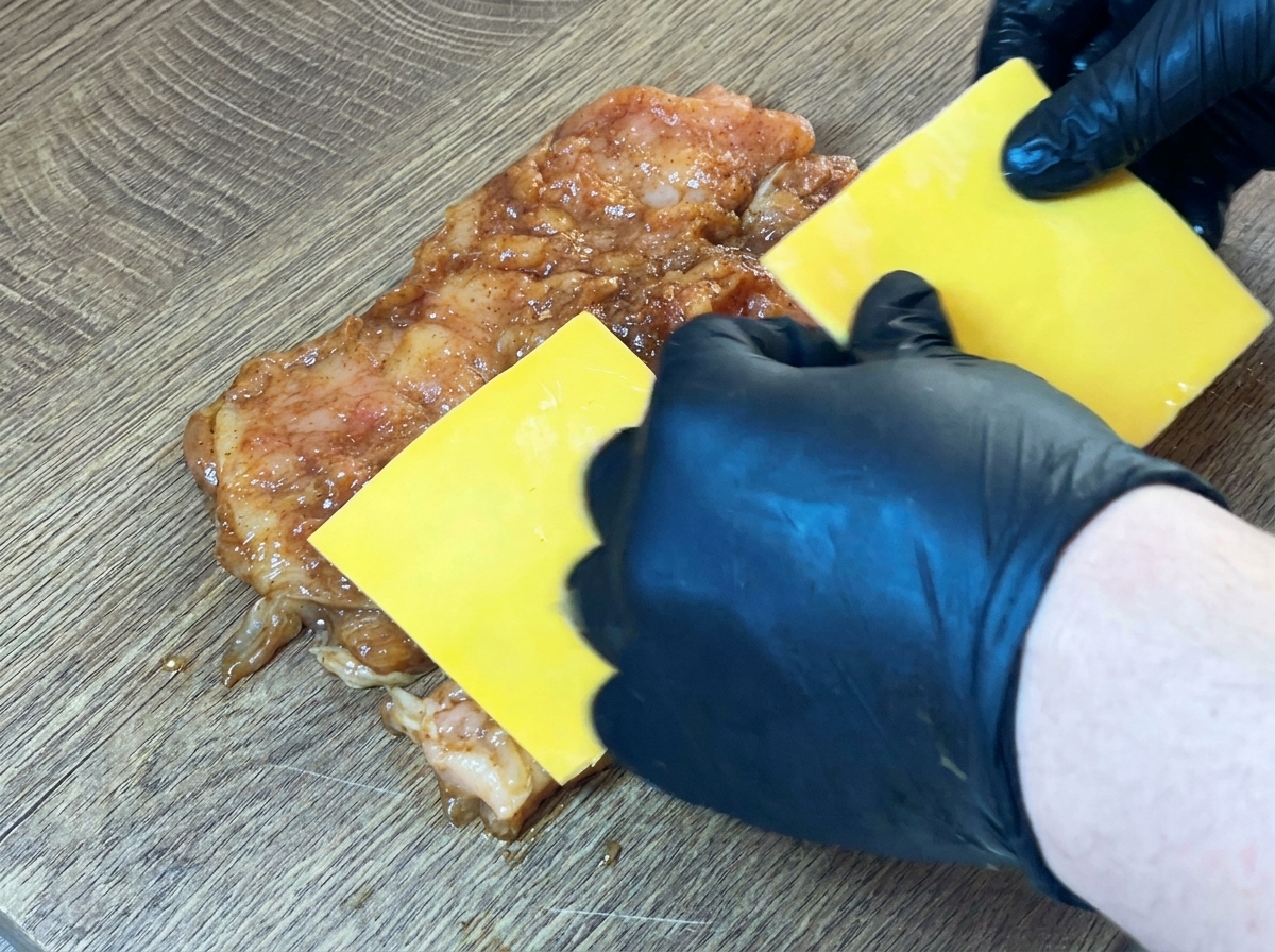 Tranches de fromage jaune placées au centre du blanc de poulet cru et mariné.