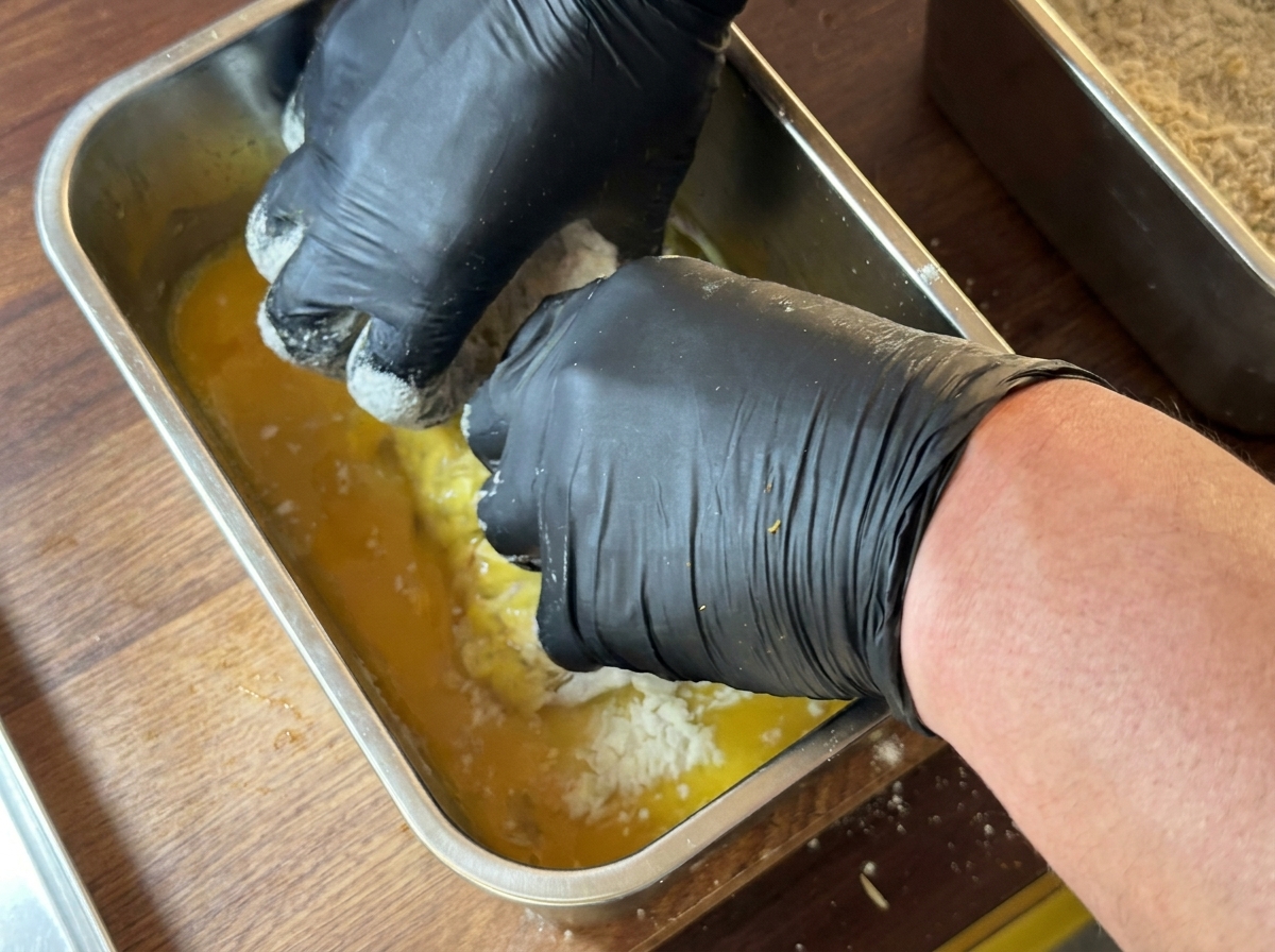 Morceau de blanc de poulet complètement immergé dans un récipient contenant de lœuf battu jaune.