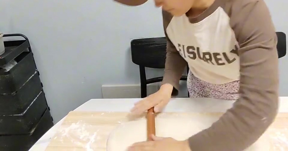 Une personne utilisant un rouleau à pâtisserie en bois pour aplatir un bloc de pâte sur une planche en bois farinée.