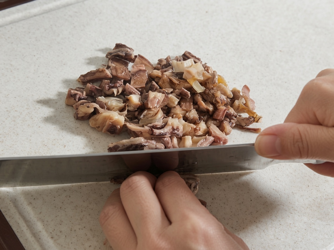 Des mains utilisant un grand couteau pour hacher des champignons shiitake réhydratés et des morceaux de poulpe sur une planche à découper blanche.