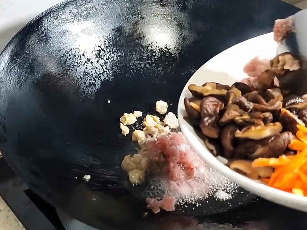 Champignons shiitake tranchés et aromates ajoutés au porc fondu dans le wok.