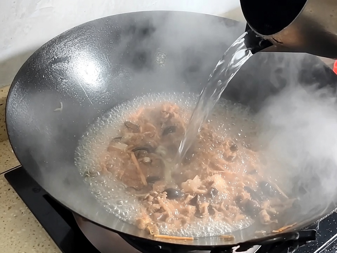 De leau est versée dans le wok avec le porc et les champignons sautés pour former le bouillon.