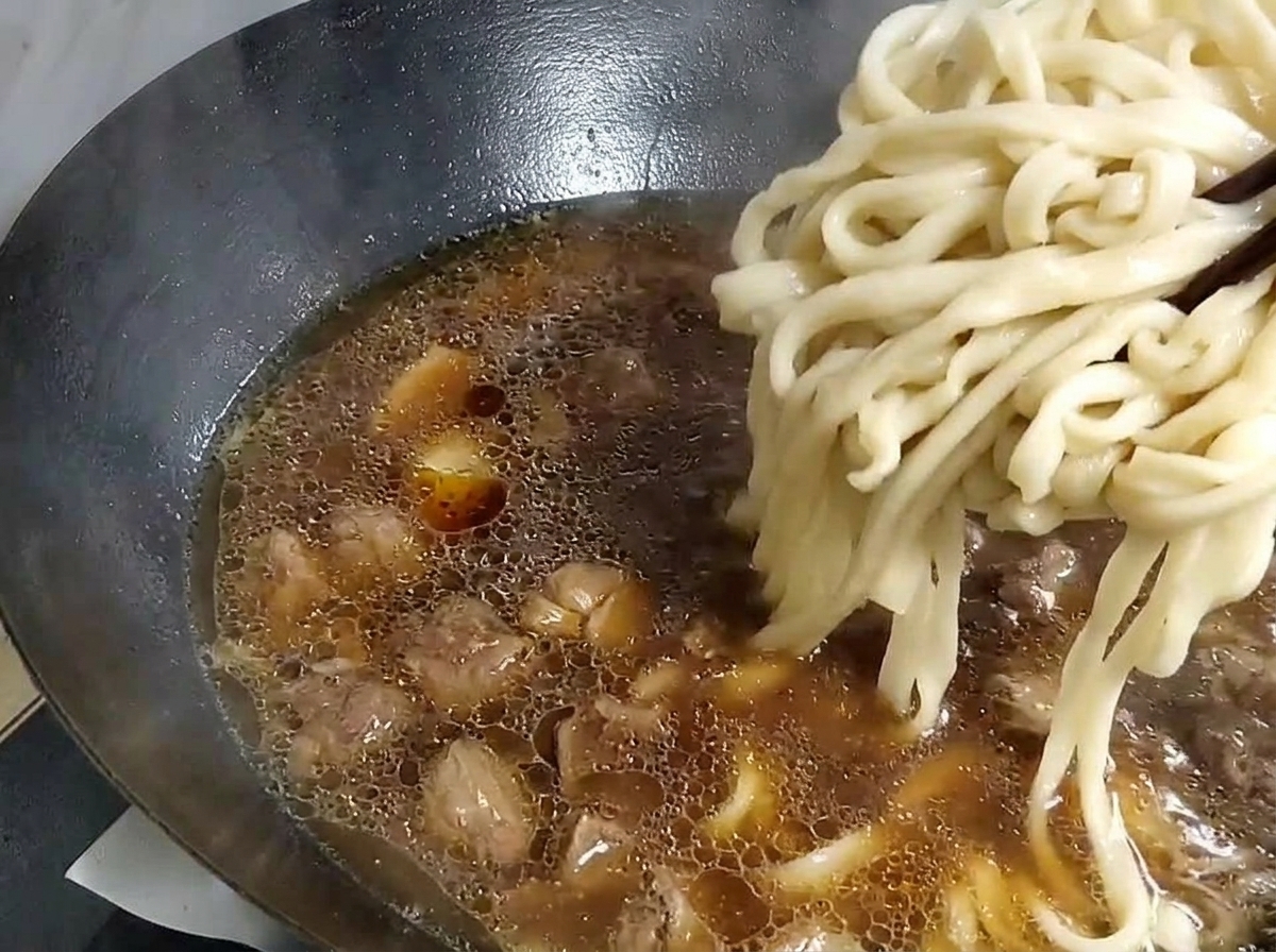 Nouilles épaisses soulevées avec des baguettes dune casserole deau et placées dans un wok avec la base de soupe.