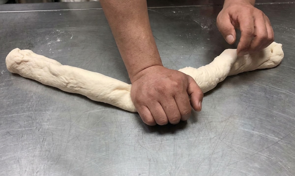 Pâte étirée en un long boudin sur une surface en acier inoxydable.