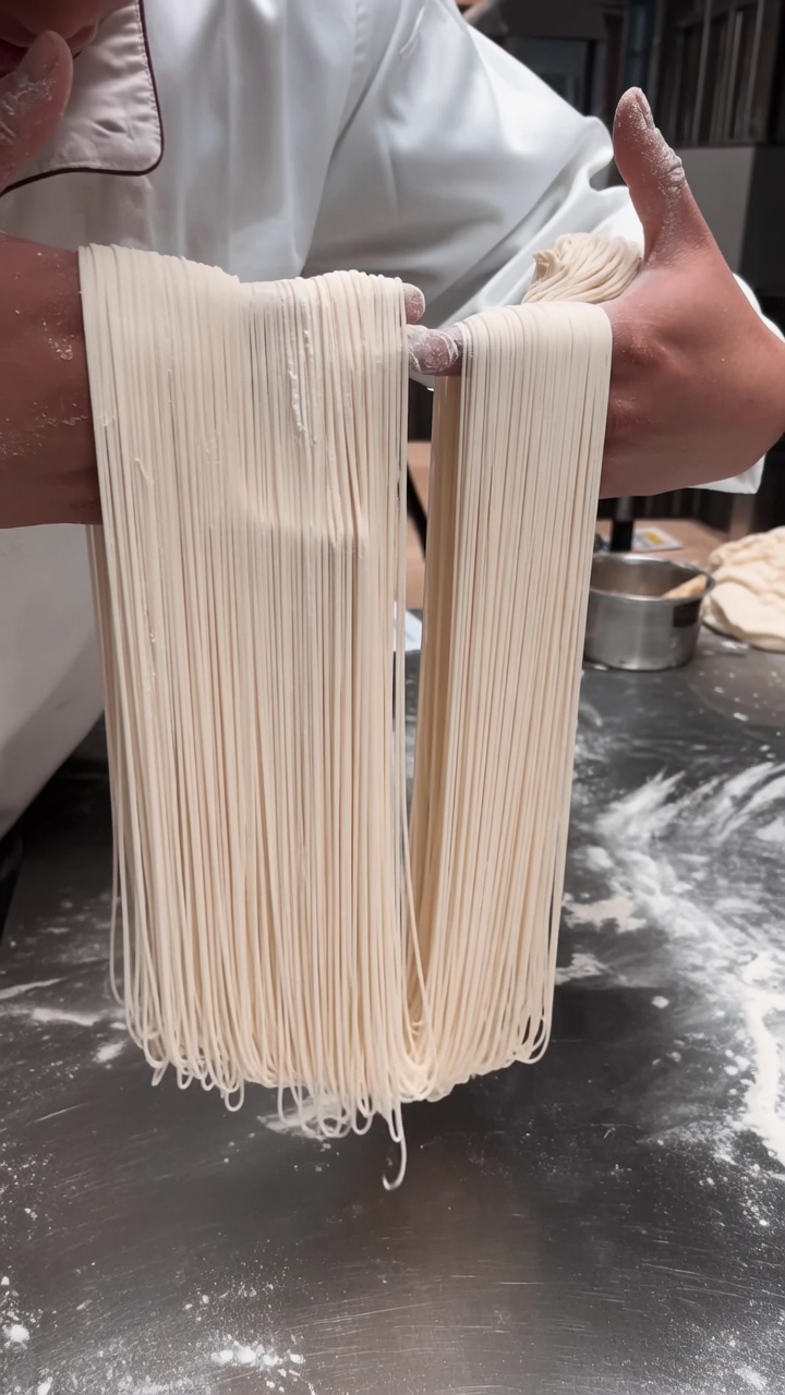 Une généreuse portion de nouilles étirées, fines comme des cheveux, suspendues avec élégance entre les mains du chef.