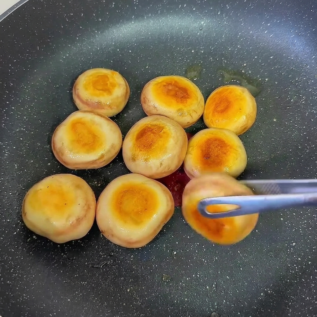 Chapeaux de champignons farcis aux crevettes en train de dorer dans une poêle.