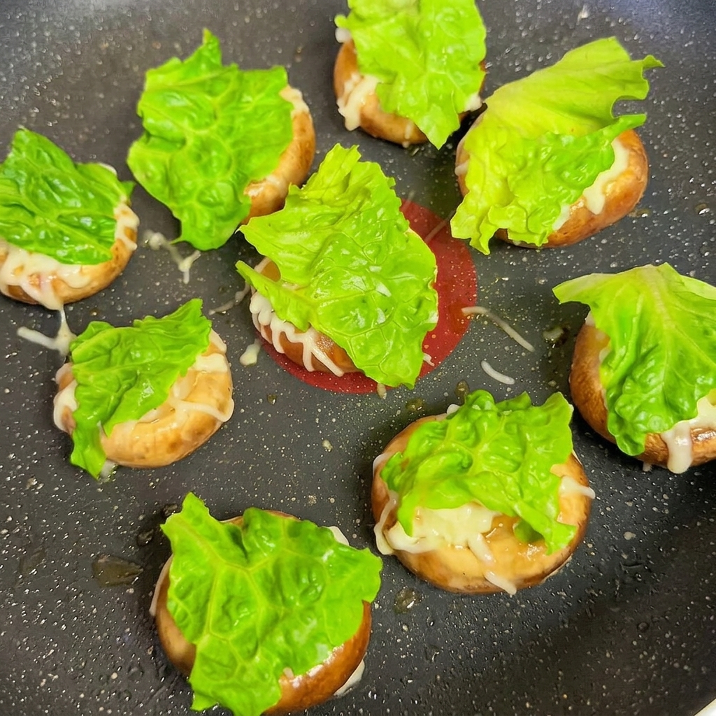 Chapeaux de champignons garnis de laitue et de morceaux de fromage dans une poêle.