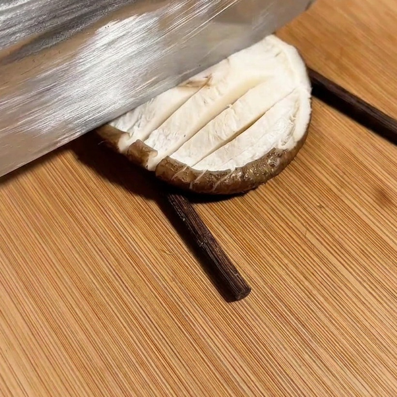Un couteau entaillant un champignon en quadrillage, placé entre deux baguettes.