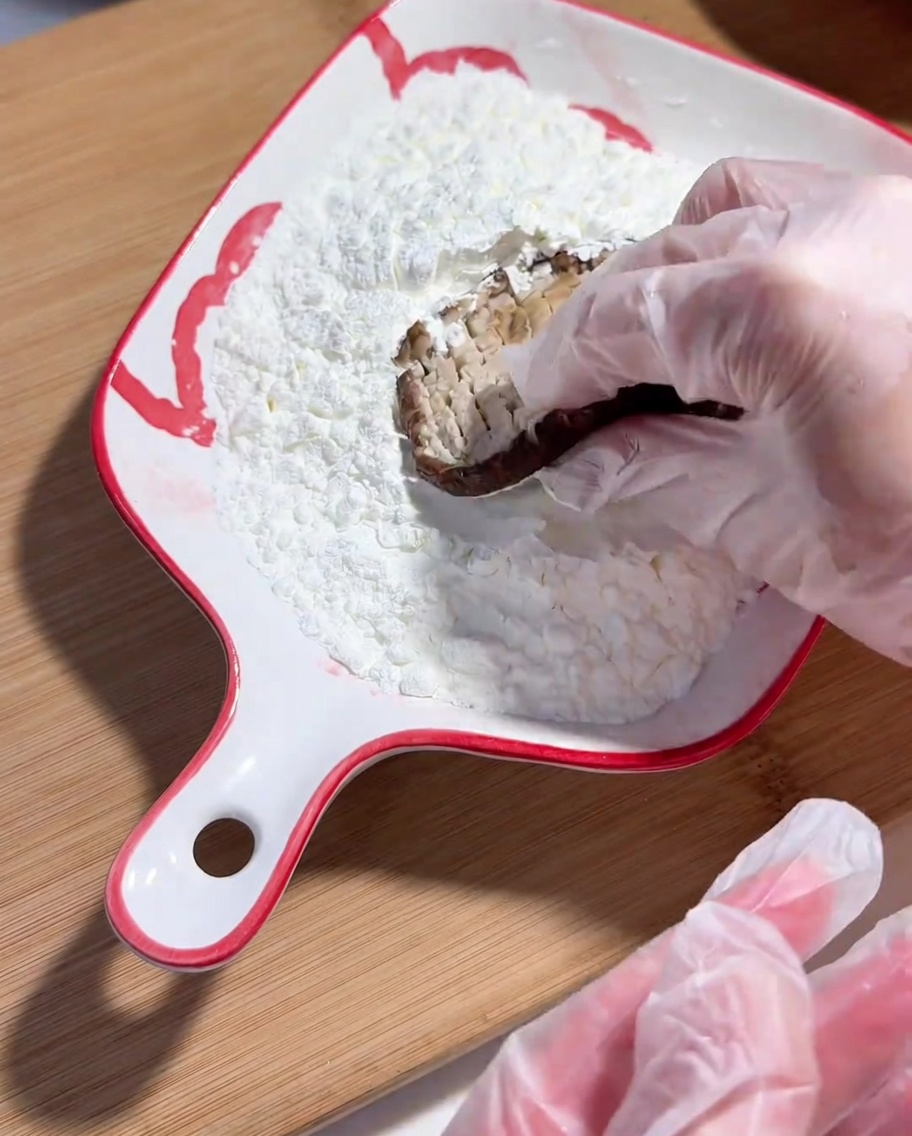 Main gantée de plastique trempant la face entaillée du shiitake dans de la fécule de maïs.