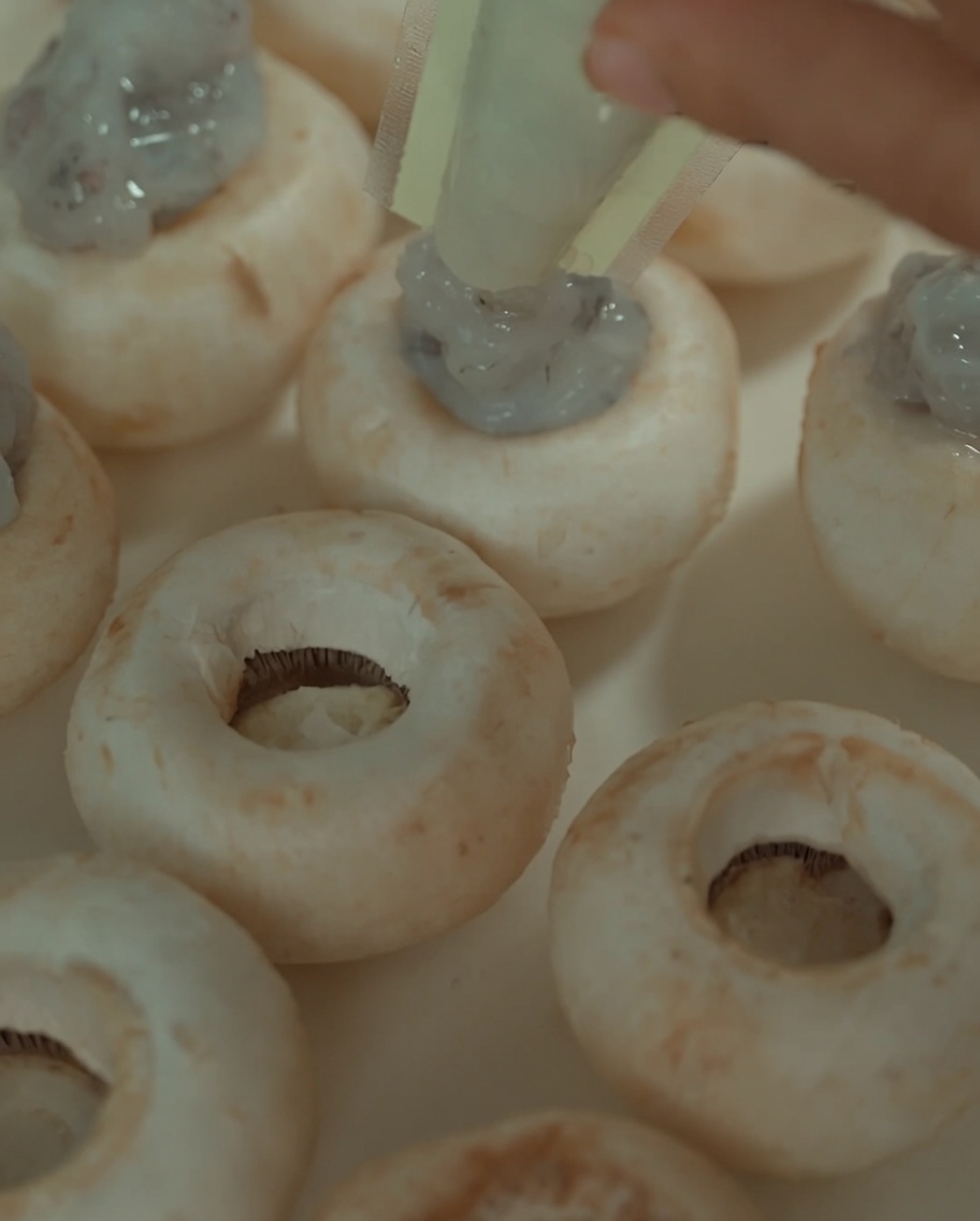 Pâte de crevettes versée à partir dun sac en plastique dans les centres creux des chapeaux de champignons cuits.