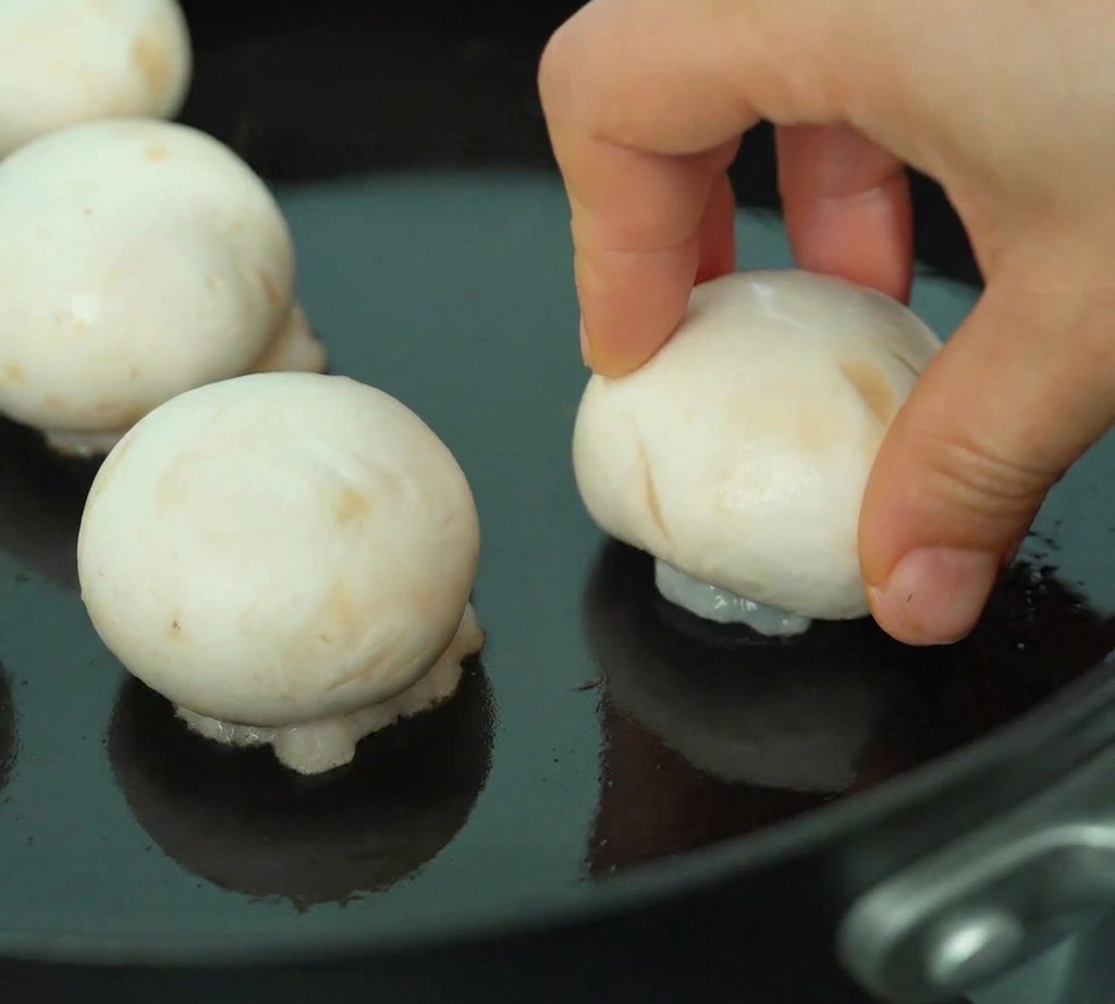 Chapeaux de champignons farcis aux crevettes saisis dans une poêle, côté farce doré vers le bas.