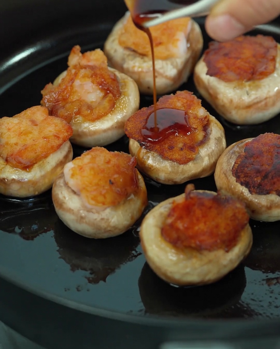 Verser un mélange de sauce soja et de jus de champignon sur les champignons farcis aux crevettes dans une poêle.