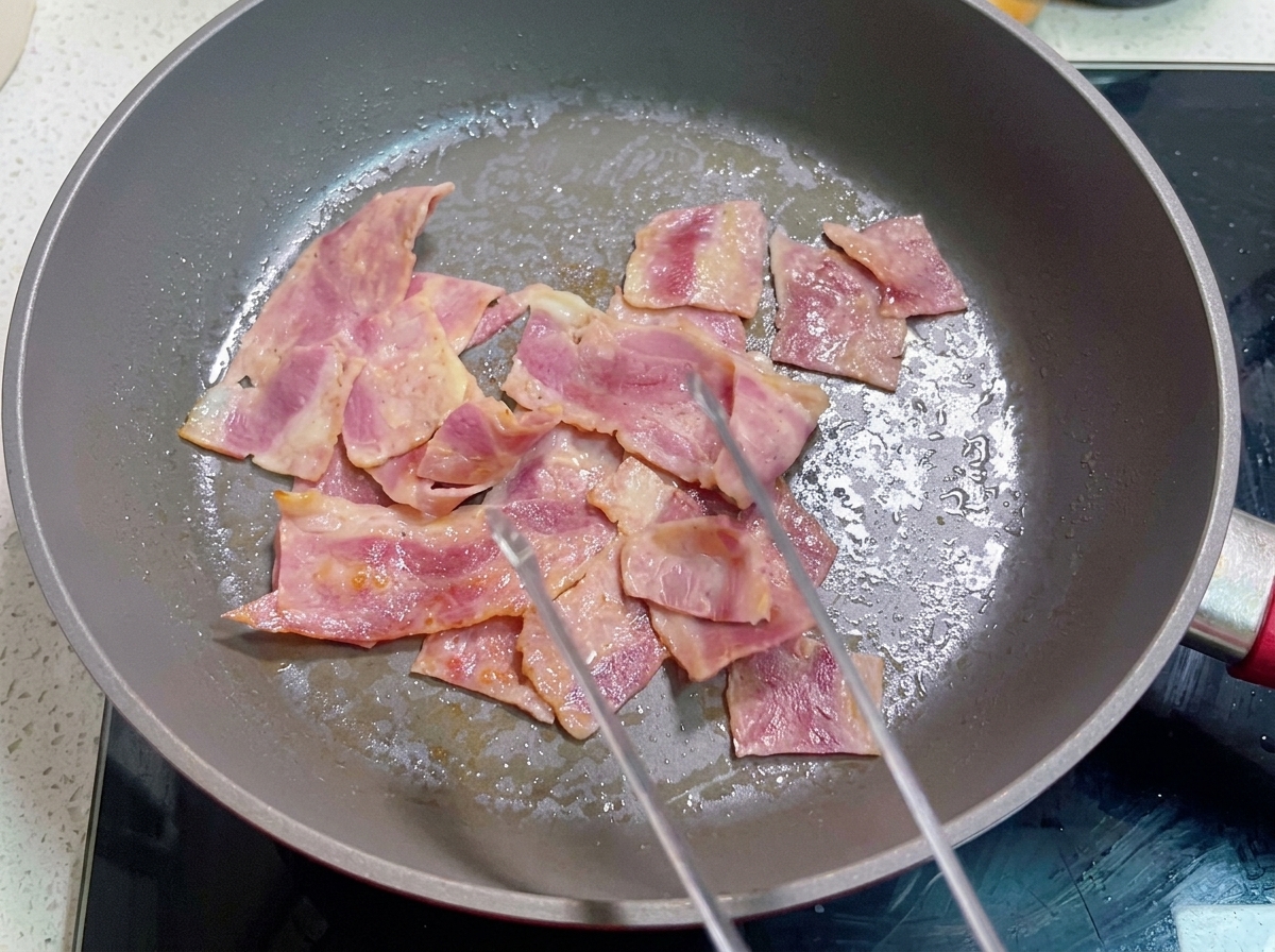 Une poêle contenant du bacon cuit sur lequel le mélange dœufs battus est versé.
